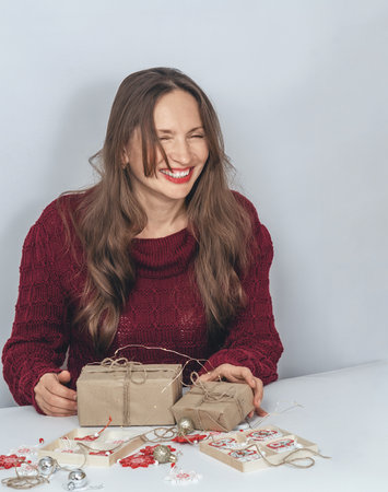 Woman laughing with eyes closed while preparing Christmas presents next to twinkling lights. Holiday themeの写真素材