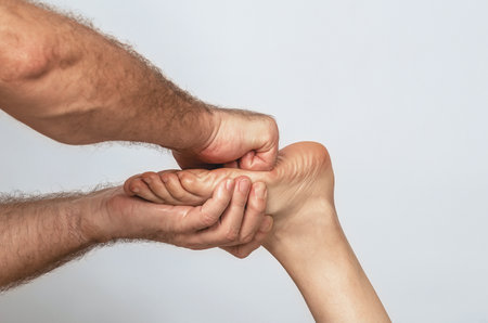 Male strong hairy hands embrace female fingers and massage base of foot. Relaxing procedures in salonの写真素材
