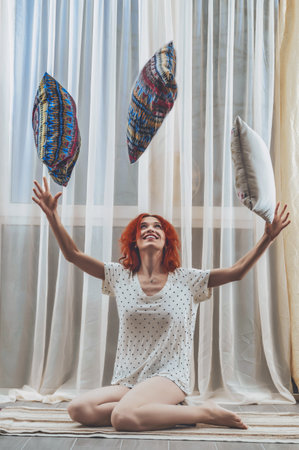 Red-haired woman sits on the floor in room, throws pillows upの写真素材