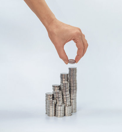 Silver coin in female fingers over column coins. Saving money, investment business concept. White backgroundの写真素材