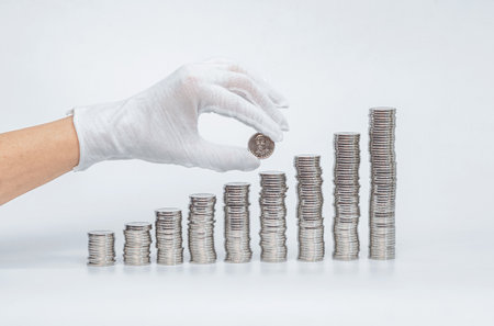 Business woman's hand in white glove puts coin in stack. Concept of finance, investment, savings and bankingの写真素材