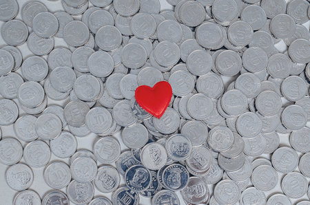 Love of money. Red heart on background of silver coins. Concept of saving, wealth, investment or charityの写真素材