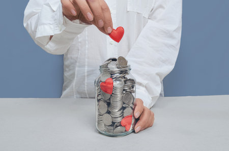 Red heart in woman's hands over jar of silver coins. Concept of wealth, investment or charity.の写真素材