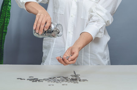 Woman in white shirt pouring coins from glass jar into palm. Concept of financial expenses