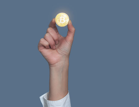 Female hand holding golden bitcoin on gray background. Cryptocurrency, finance and technologyの写真素材