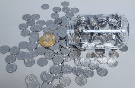 Bitcoin against silver coins spilling from glass jar. Symbol integration of cryptocurrency in modernityの写真素材