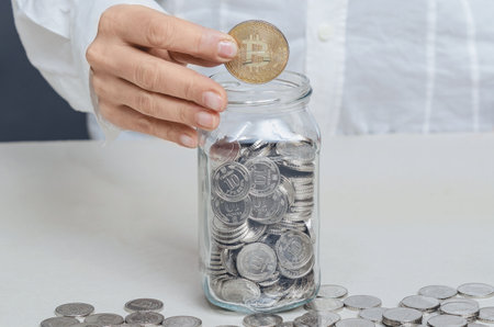 Close-up of golden bitcoin in female hands above glass jar with coins. Cryptocurrency. Digitalizationの写真素材