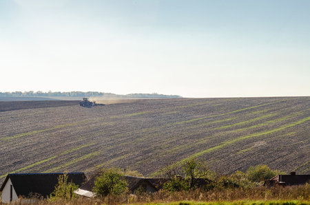 Tractor plows field, raising dust, turning over black soil in countryside. Agriculture, spring field workの写真素材