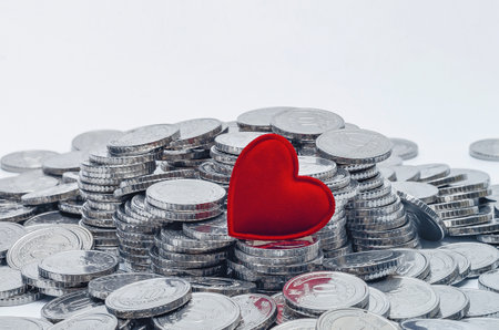 One red heart on pile of shiny coins. White background. Place for descriptionの写真素材