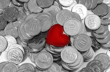 Background of silver coins with red heart in the middle. Money for well-being, pleasure or charityの写真素材