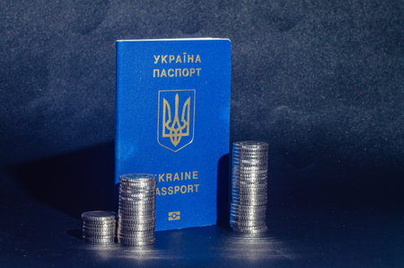 Ukrainian passport near stacks of coins. Problems of migration, war, subsidies. Dark blue backgroundの写真素材