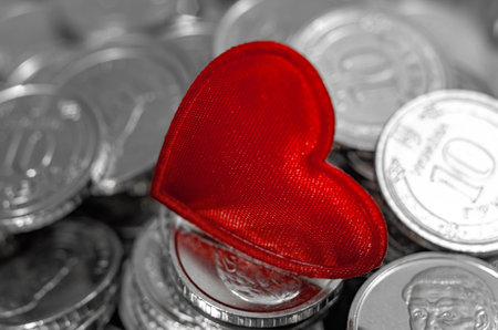 Macro Red heart on blurred background of coins. Money for travel, jewelry, pleasure or charity. Valentine's Dayの写真素材