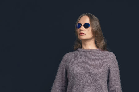Serious woman with long hair wearing dark blue glasses posing on dark blue background. Mysterious atmosphereの写真素材