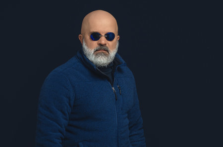 Bald bearded man in dark blue sweater and glasses. Looking at camera. Studio black backgroundの写真素材