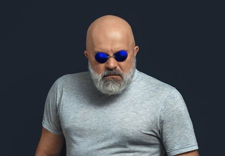 Broad shouldered man with gray beard wearing dark glasses looking at camera.の写真素材