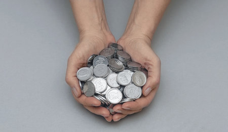 Pile silver coins in women's palms on gray backdrop. Idea of importance of social financial supportの写真素材