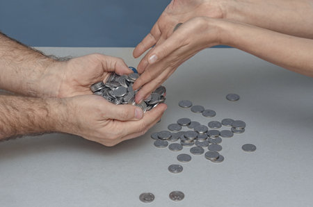 Transfer money from person to person. Female hands transfer silver coins to male hands. Gray...