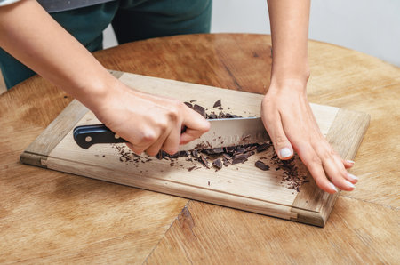 Hands with knife cutting dark chocolate on wooden boardの写真素材