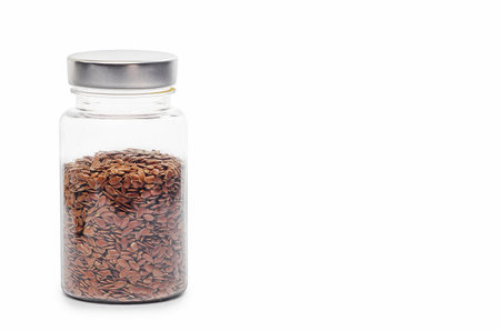 Glass jar filled with flaxseeds and metal cap on white backgroundの写真素材