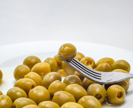 Fork lifting a green olive from a plate of olives on white backgroundの写真素材