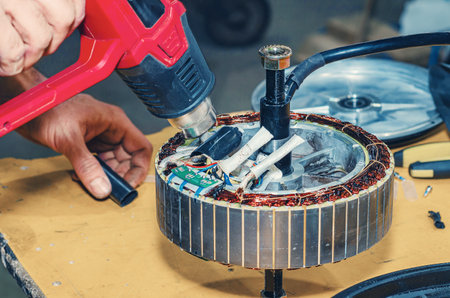 Heat gun warms up insulation of bicycle's electric motor. Repair of electric bicycles. Hands of...
