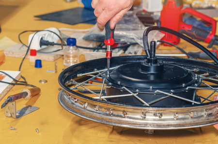 Unscrewing cover of electric motor with screwdriver. Repair of electric bicycles. Table workshop backgroundの写真素材