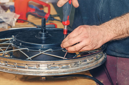 Bicycle mechanic tightens cover on electric motor using screwdriver. Electric bicycle repair. Workshopの写真素材