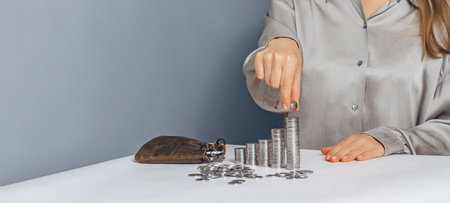 Woman in silver blouse puts coins on stacks. Leather bag with coins. Wealth, money, accounting, finance, investment. Copy spaceの写真素材