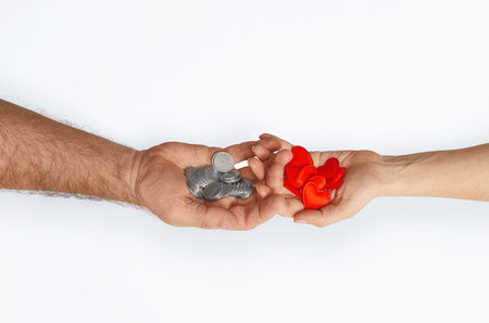 Male hand with coins crosses with female hand with red hearts on white background, isolated. Concept of love and money, agreementの写真素材