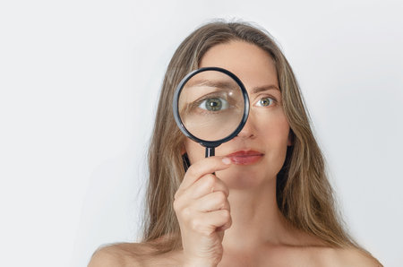 Adult woman with magnifying glass looking at camera with big zoom eye, smiling. Verification, choice strategy conceptの写真素材