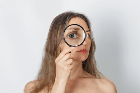 Long-haired woman with magnifying glass looking at camera with big zoom eye, checking authenticity. Verification, choice conceptの写真素材