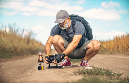Male photographer crouched down and holding camera in the middle of field road. Taking pictures of Turkish coffee maker. Concept of travel and outdoor adventures.の写真素材