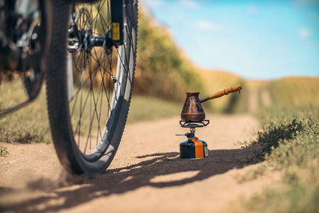 Bicycle wheel near Turkish coffee maker on portable gas stove on trail. Blurred field landscape. Making coffee.の写真素材