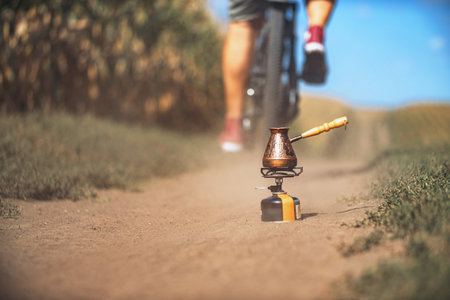Turkish coffee maker on portable gas stove on trail. Outdoor recreation. Blurred background bicycle...