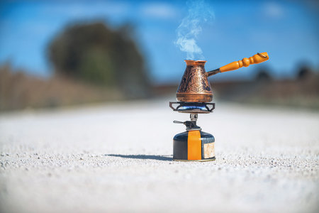 Copper Turkish coffee pot with wooden handle on portable gas stove brews coffee. Sky background. Drinking coffee on natureの写真素材