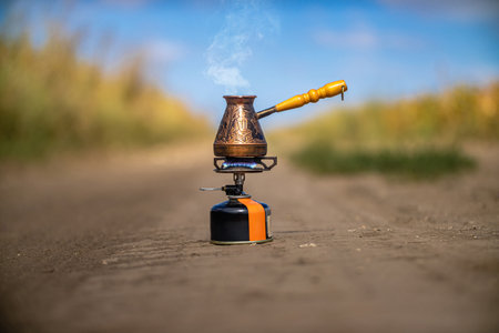 Copper Turkish coffee pot with wooden handle on small portable gas stove brewing coffee. Coffee drinking in natureの写真素材