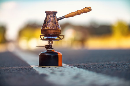 Copper Turkish cezve for making coffee stands on tourist gas burner in the middle of highway. Concept of need for coffee. Copy space pictureの写真素材