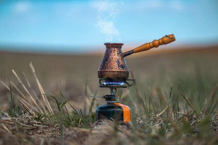 Fragrant coffee steams in copper engraved coffee pot on gas burner against blue blurred sky. Idea of...