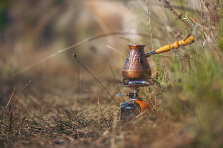 Coffee is prepared in copper coffee pot on manual coffee maker gas burner. Concept of rest and break, morning routine on hike. Tourism concept.の写真素材