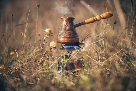 Making coffee in Turkish cezve on gas burner for camping. Fire with blue flame and steam over hot delicious coffee among these. Morning coffee in natureの写真素材