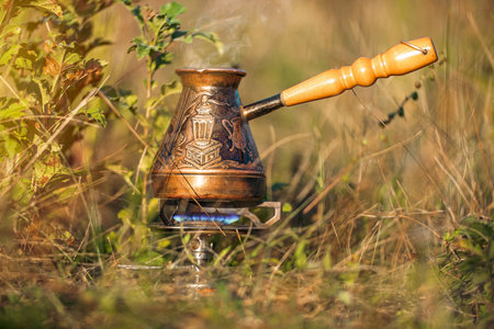 Brewing coffee in Turkish cezve on gas burner for camping. Fire with blue flame and steam over hot delicious coffee in the wild. Evening coffee with friendsの写真素材