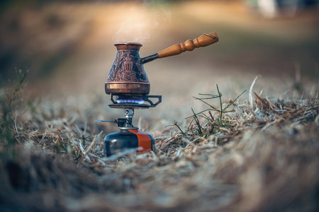 Boiling coffee in Turkish cezve on camping gas burner. Fire with blue flame and steam over hot delicious coffee. Luxury nature camping conceptの写真素材