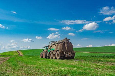 Rear view of agricultural tractor with manure standing on green field. Manure as fertilizer in agricultureの写真素材
