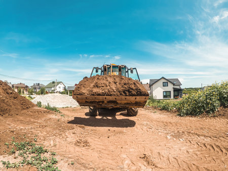 Big yellow tractor-loader is transporting earth. Preparation of construction site. Leveling landscapeの写真素材