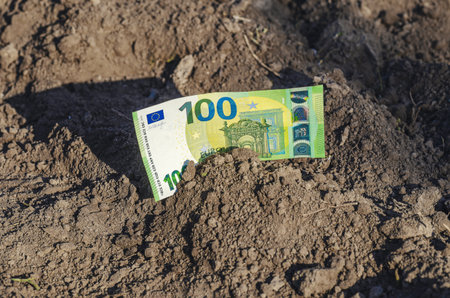 Photo of 100 euro banknote on surface of black soil. Concept of business, savings, growth, investment. Environmental theme.の写真素材