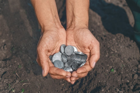 Human palms with silver coins on natural background of plowed black soil. Concept of conservation, investment in future, ecology, agriculture.の写真素材