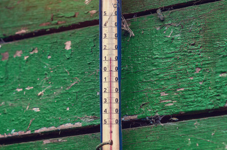Thermometer for measuring air temperature on a painted green cracked wooden wall shows temperature of 12 degrees Celsius. Old street thermometer.の写真素材