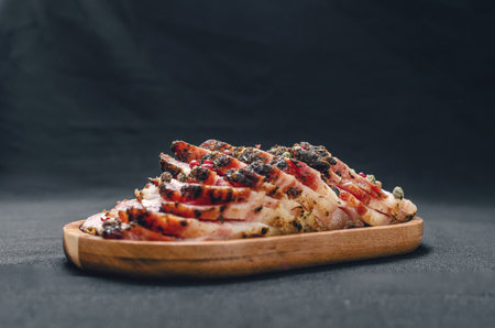 Fragrant slices of baked pork belly on a wooden board, sprinkled with colored peppercorns. Black background. Side view Meat preparation concept.の写真素材