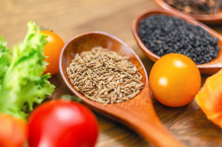 Wooden spoon of cumin seeds close-up. Cumin seeds in spoon on wooden surface. Lettuce, black sesame,...
