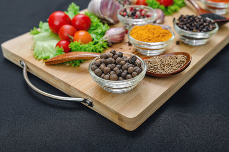 Allspice in bowl close-up among various spices, sesame, cloves and vegetables, cherry tomatoes,...